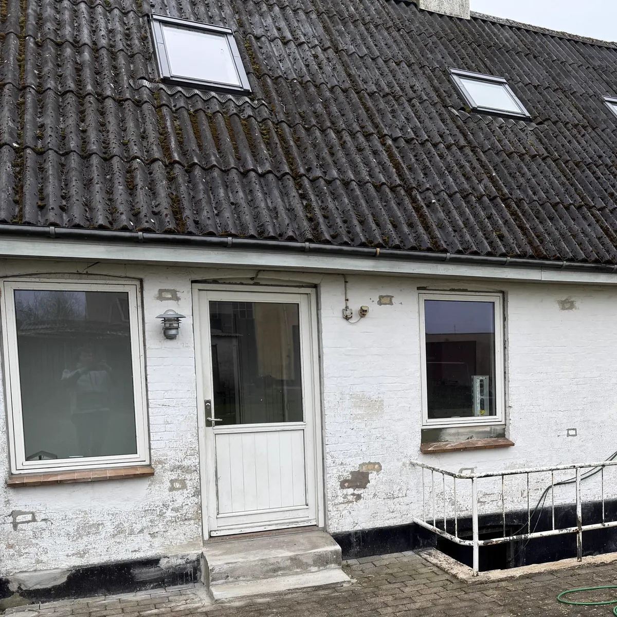 Hus på Sjælland før tagrens: tagfladen er mørk og tilgroet med mos og alger, og den hvidkalkede facade står grå og stribet