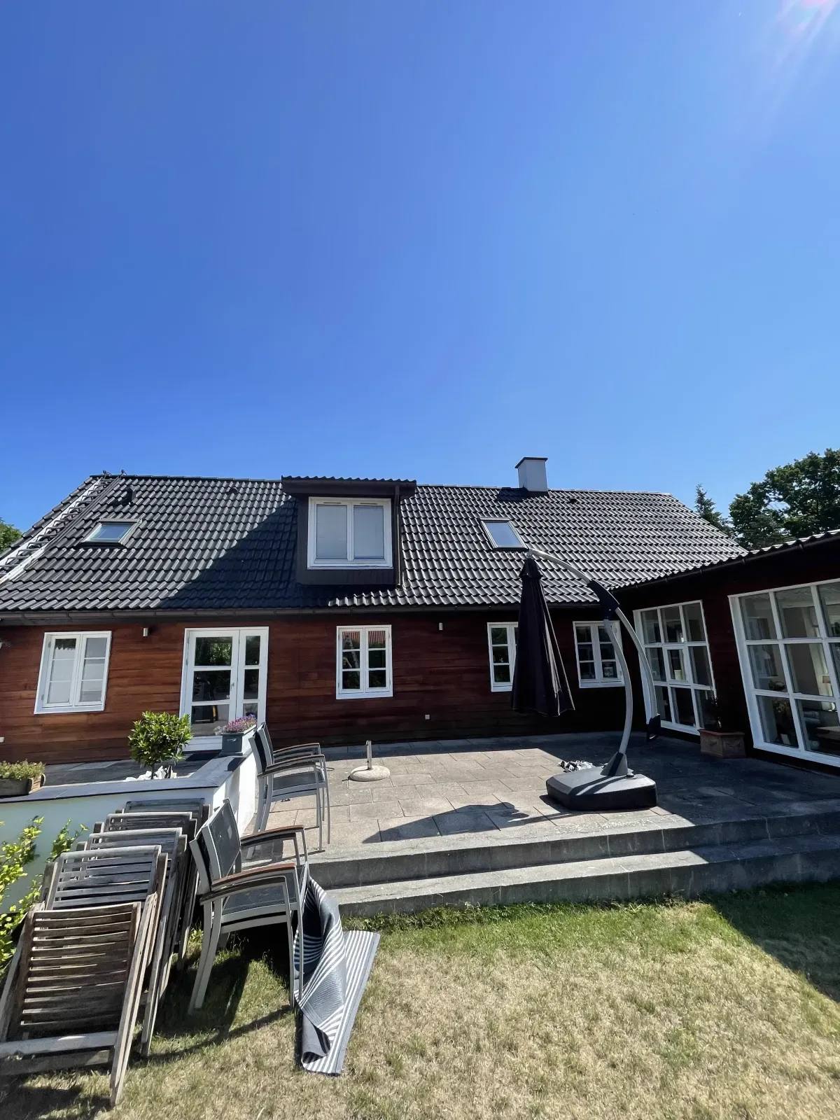 Villa på Sjælland set fra havesiden med ensartet mørkt tag efter tagrens og to lag tagmaling, under en skyfri sommerhimmel