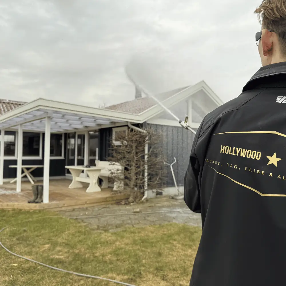 Medarbejder i Hollywood-jakke sprøjter med teleskoplanse taget på et mørkt hus med hvid pergola og træterrasse